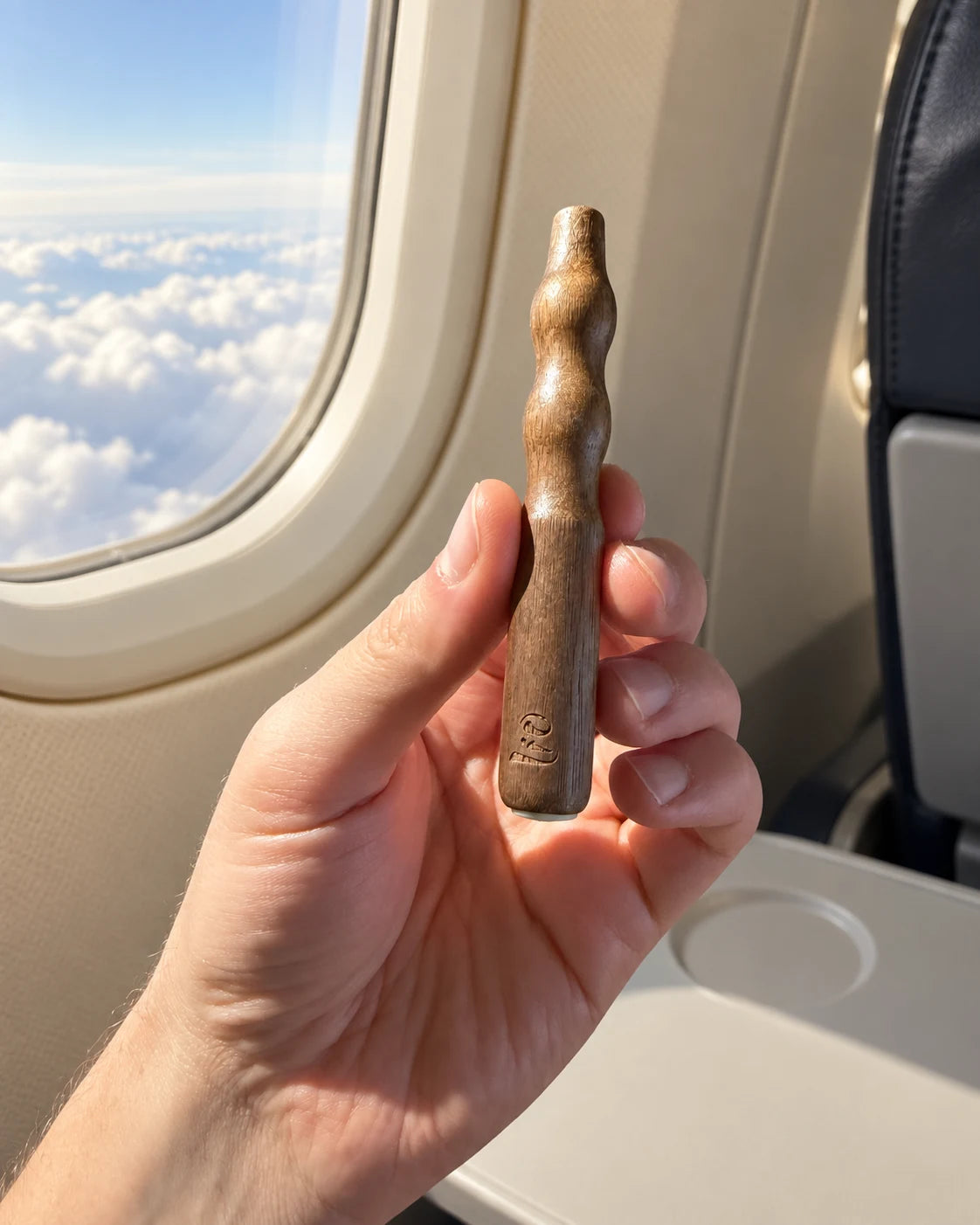 Një dorë mban pajisjen prej druri Lio pranë dritares së aeroplanit, mbi re